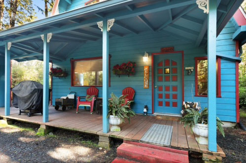 A colorful blue house with a welcoming porch, featuring red chairs, potted plants, and a grill.