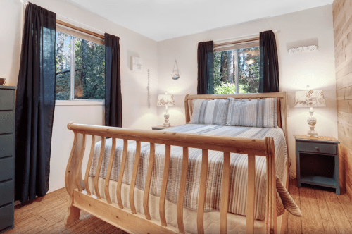 Cozy bedroom with a wooden bed, striped bedding, and large windows overlooking a forested area.