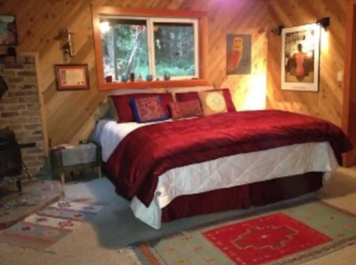 Cozy bedroom with a large bed, wooden walls, a fireplace, and decorative rugs. Warm lighting creates a welcoming atmosphere.
