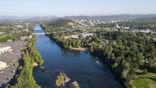 Aerial view of a river winding through a city, surrounded by greenery and hills in the background.
