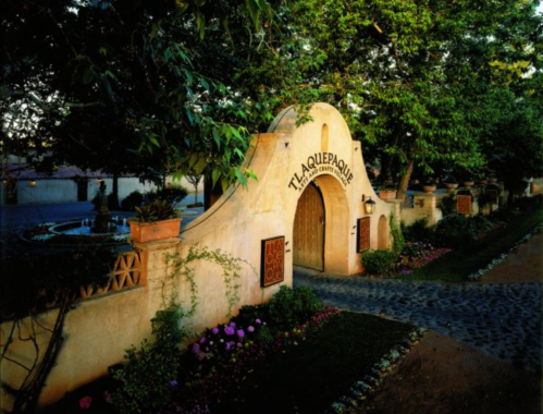 A charming entrance with an arched doorway, surrounded by lush greenery and colorful flowers, leading to a serene courtyard.