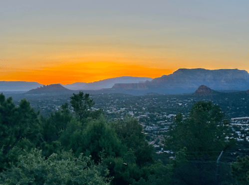 A scenic sunset over a mountainous landscape, with vibrant orange and yellow hues illuminating the sky.