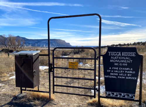 Gate entrance to Yucca House National Monument, with a scenic view of mountains and open fields in the background.