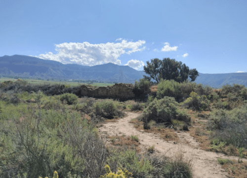 A scenic view of a rugged landscape with mountains, a cloudy sky, and remnants of a stone structure surrounded by vegetation.