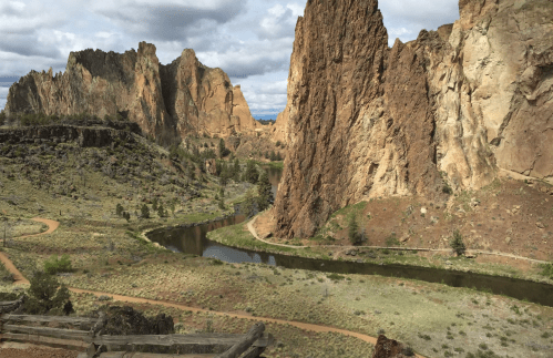 A scenic view of rugged rock formations beside a winding river, surrounded by green vegetation under a cloudy sky.