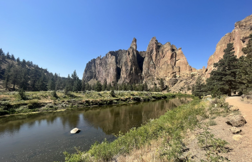 A serene landscape featuring a river, lush greenery, and towering rock formations under a clear blue sky.