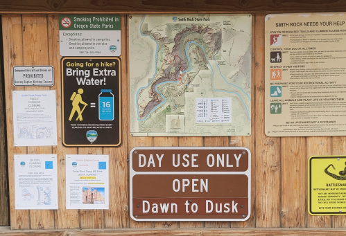 Information board at Smith Rock State Park with maps, rules, and reminders about water and park hours.