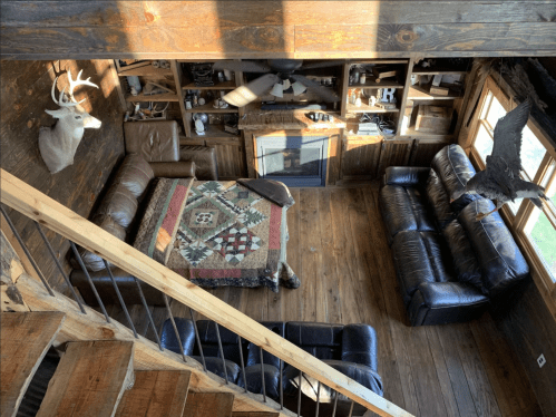 Cozy living room with wooden walls, leather sofas, a quilt, and rustic decor, viewed from above.