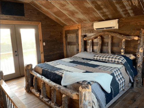 Cozy bedroom with a rustic log bed, quilted bedding, and large windows overlooking a natural setting.