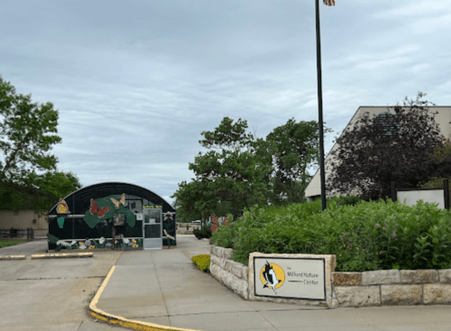 Entrance to the Wild Nature Center, featuring a colorful mural and landscaped greenery under a cloudy sky.