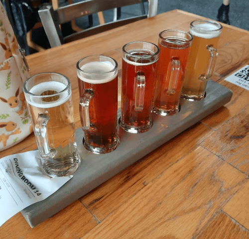 A wooden flight board with five small glasses of different beers on a table.