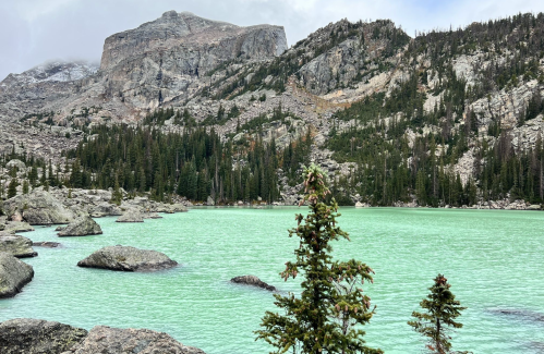 A serene landscape featuring a turquoise lake surrounded by rocky terrain and evergreen trees under a cloudy sky.