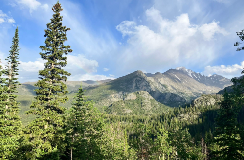 A scenic view of mountains and lush green trees under a blue sky with fluffy clouds.