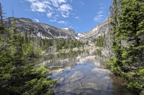 A serene mountain lake surrounded by lush greenery and rocky terrain under a clear blue sky.