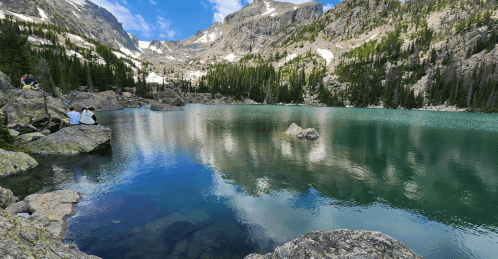 A serene mountain lake surrounded by rocky shores and lush greenery, reflecting the sky and mountains above.