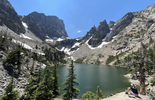 A serene mountain lake surrounded by rocky peaks and pine trees under a clear blue sky.