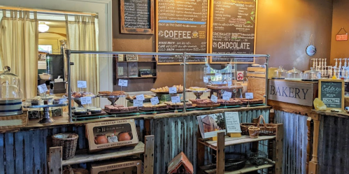 A cozy bakery display with various pastries, a chalkboard menu, and rustic wooden decor.