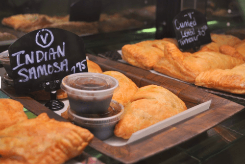 A display of Indian samosas and curried lentil pastries with dipping sauces on a wooden tray.