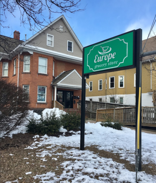 A grocery store sign reading "Europe" in front of a two-story building, with snow on the ground and trees nearby.