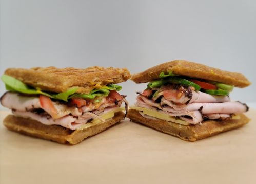 Two stacked sandwiches with layers of turkey, ham, cheese, lettuce, and tomato on a golden-brown bread.