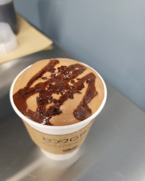 A cup of chocolate dessert topped with chocolate drizzle and sprinkles, placed on a metallic surface.