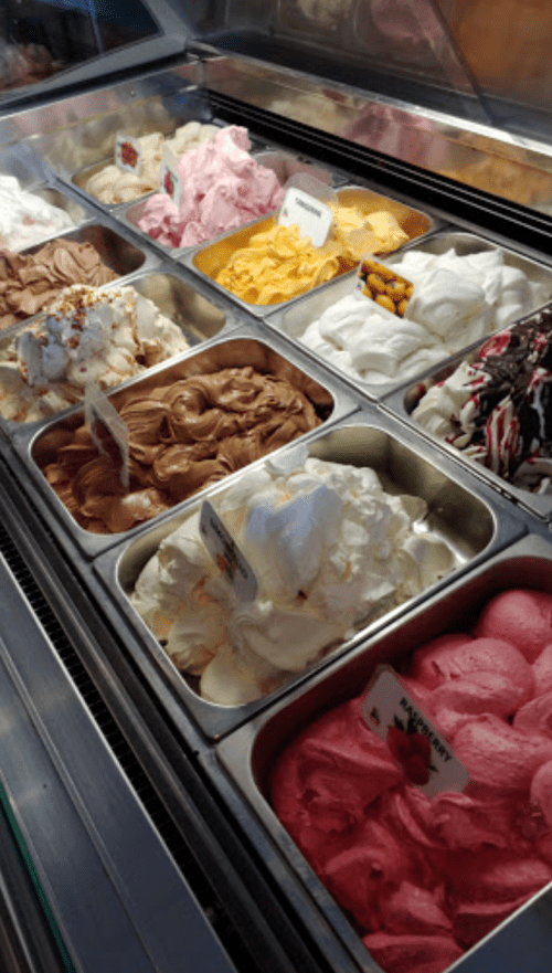 A display of various ice cream flavors in metal tubs, including chocolate, vanilla, strawberry, and more.