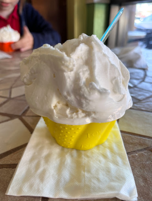 A close-up of a creamy white ice cream scoop in a yellow cup, resting on a napkin on a table.