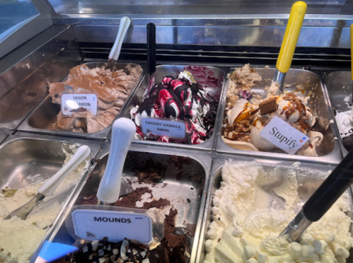 A display of various ice cream flavors in metal containers, including Cherry Vanilla Swirl and Mounds.
