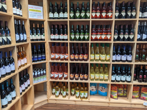 A wooden shelf displaying various bottles of wine and beverages in a tasting room.