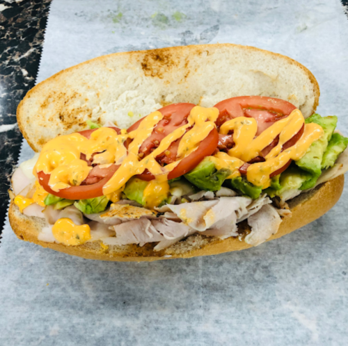 A sandwich with sliced turkey, lettuce, tomato, and drizzled with orange sauce on a toasted hoagie roll.