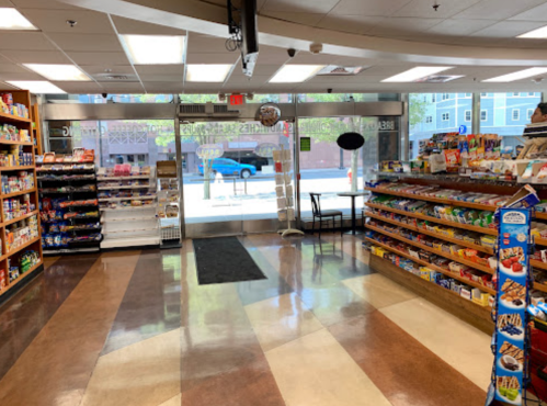 Interior of a convenience store with shelves stocked with snacks and drinks, and a large entrance visible in the background.
