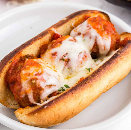 A toasted sub roll filled with meatballs, marinara sauce, and melted cheese, garnished with herbs.