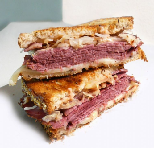 A stacked sandwich with layers of corned beef, sauerkraut, and melted cheese on toasted bread.