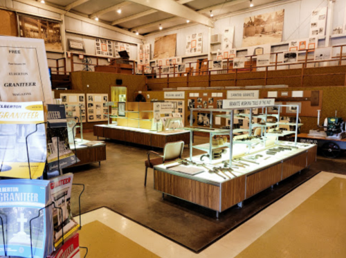 Interior of a museum exhibit featuring displays of granite tools and historical photographs, with seating areas.