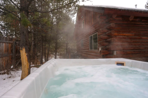 A steaming hot tub in a snowy outdoor setting, with a rustic wooden cabin in the background.