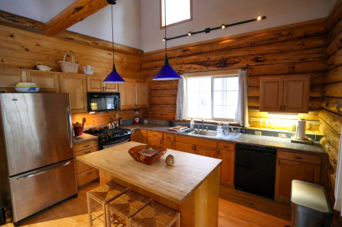Cozy kitchen with wooden beams, stainless steel appliances, blue pendant lights, and a central island with stools.