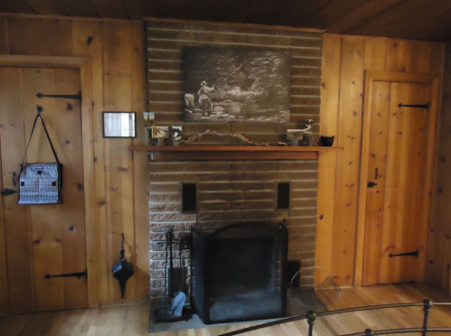 Cozy wooden room featuring a stone fireplace, a vintage photo above, and two doors on either side.
