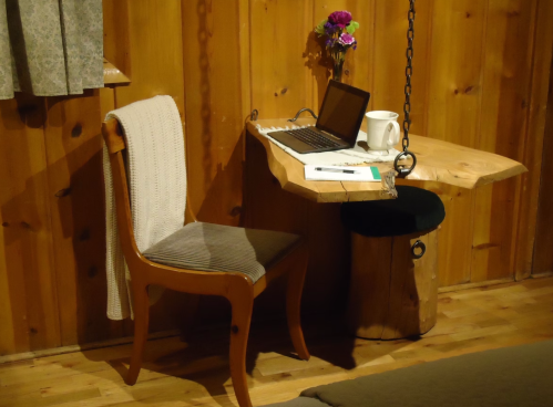 A cozy wooden workspace with a chair, laptop, mug, and a small flower vase against a rustic wooden wall.