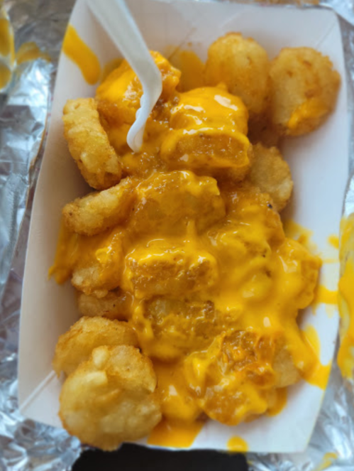 A container of tater tots smothered in melted cheese sauce, with a plastic fork resting on top.