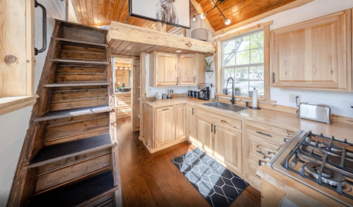 Cozy kitchen with wooden cabinets, a staircase, and natural light streaming in through large windows.