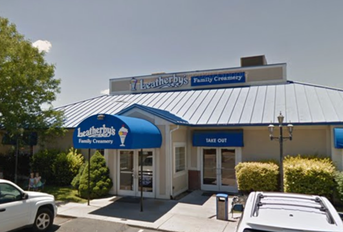 Exterior of Leatherby's Family Creamery, featuring a blue awning and a take-out sign, surrounded by greenery.