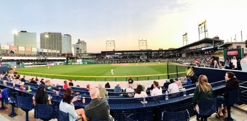 A panoramic view of a baseball stadium filled with fans, with a sunset backdrop and players on the field.