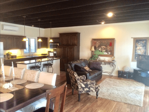 Cozy living space with a dining area, dark wood furniture, and a kitchen in the background, featuring warm lighting.