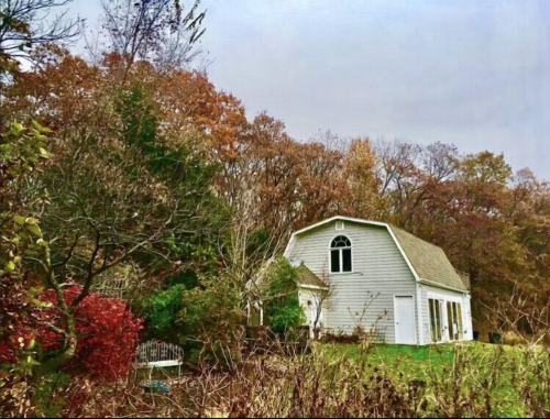 A quaint gray house surrounded by colorful autumn foliage and trees under a cloudy sky.