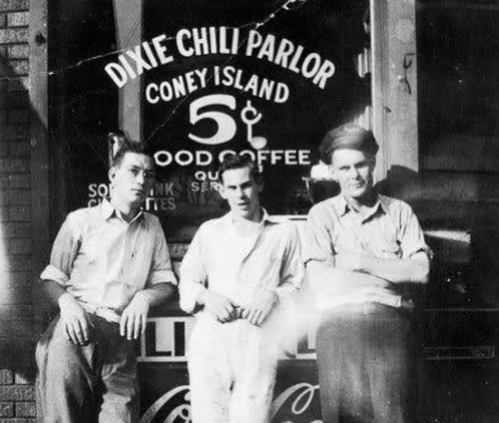 Three men stand outside the Dixie Chili Parlor, with a vintage sign advertising coffee and food.