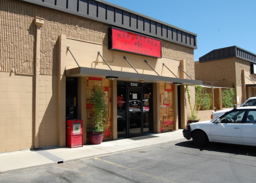 Exterior of Meriwether Cider Co. with a red sign, plants, and parked cars in front on a sunny day.