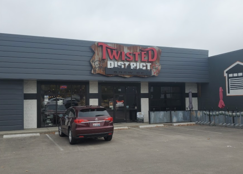 Exterior of Twisted District Brew Co. building with a sign, featuring a parked car in front and cloudy skies.
