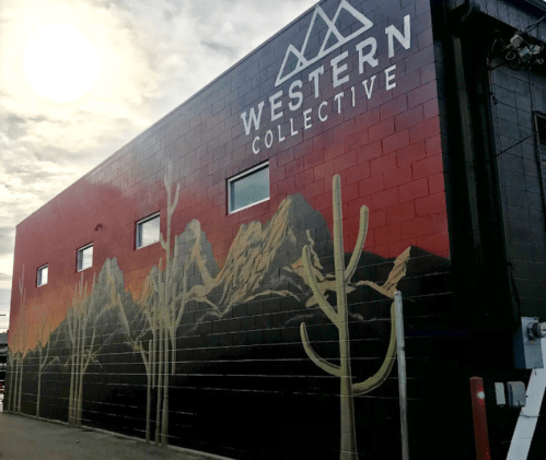 Mural on a building featuring mountains and cacti, with a sunset sky and "WESTERN COLLECTIVE" text at the top.