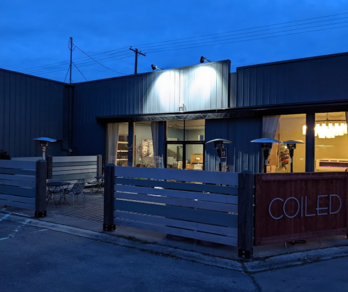A modern building with a sign reading "COILED," featuring outdoor seating and warm lighting at dusk.