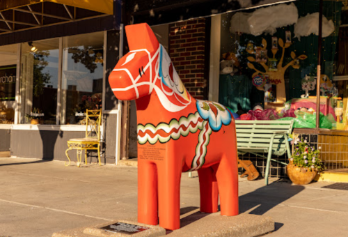 A colorful, decorative horse statue stands outside a shop, with vibrant patterns and a playful design.